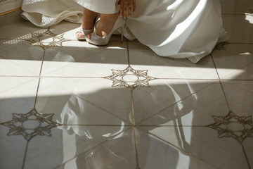 Bride takes on wedding shoes standing on marble floor