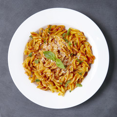 Aerial view of a dinner dish full of tomato and basil fusilli pasta on a rustic slate background