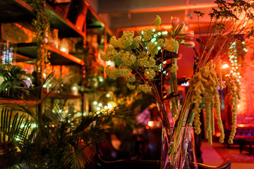 Branches of greenery stand in high vase on dinner table