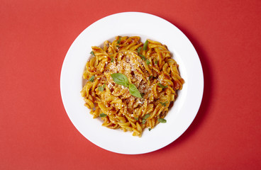 Aerial view of a dinner dish full of tomato and basil fusilli pasta on a bright red background