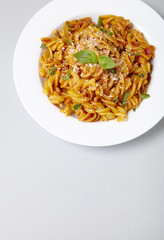 A dinner dish full of tomato and basil fusilli pasta on a pastel grey background with blank space below