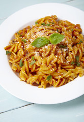 A dinner dish full of tomato and basil fusilli pasta on a blue wooden table background