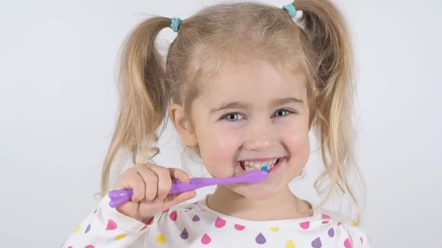 Cute little girl with pigtails diligently brushing his teeth. In the hand of the girl has toothbrush. Cheerful girl looking into the camera.