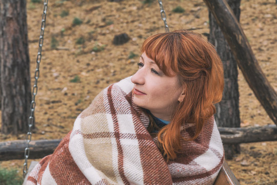 Beautiful red haired young woman with blanket on a bench at the autumn park. Coloring and processing photo