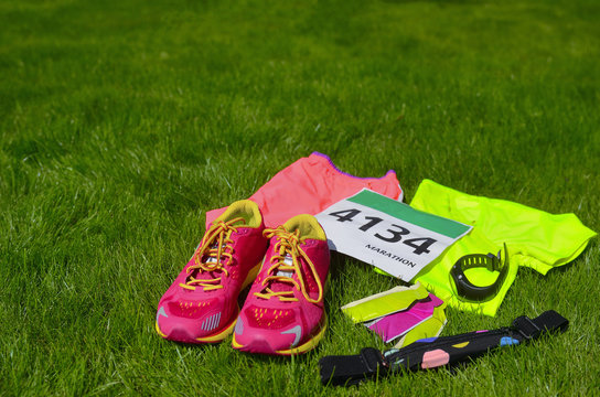 Running shoes, marathon race bib (number), runners gear and energy gels on grass background, sport, fitness and healthy lifestyle concept
