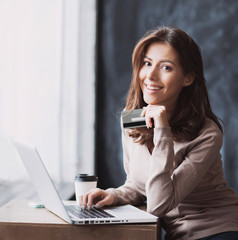 Young woman holding credit card and using laptop computer. Online shopping concept