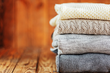 Obraz na płótnie Canvas Stack of knitted winter clothes on wooden background, sweaters, space for text