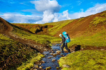 Travel to Iceland. Beautiful Icelandic landscape with hiker passes through creek, mountains, sky and clouds. Trekking in national park Landmannalaugar