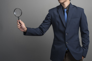 Close up of businessman in blue suit holding magnifier on gray b