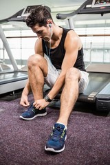 Fit man sitting on treadmill and tying the shoelace