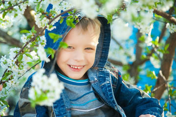 Close up portrait of smiling beautiful child face age of 7 years old playing hide and seek among branches of spring tree in blossoms.