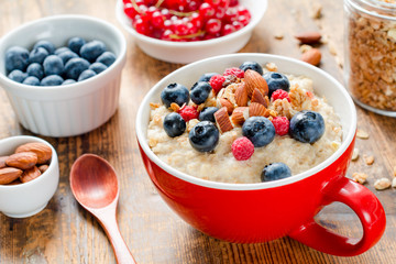 Oatmeal porridge with fresh blueberries, raspberries, almonds and muesli on red plaid textile. Close up. Healthy food, healthy breakfast, healthy lifestyle concept