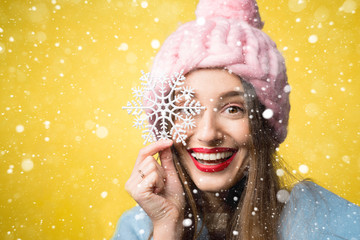 Happy woman in colorful winter clothes holding a beautiful snowflake standing on the yellow background. Happy winter concept