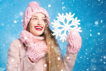 Winter portrait of a beautiful woman in knitted pink scurf, gloves and hat with snow flake on the blue background