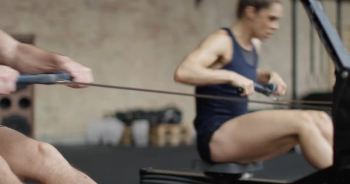 Fit man and woman exercising in gym, working out on rowing machine