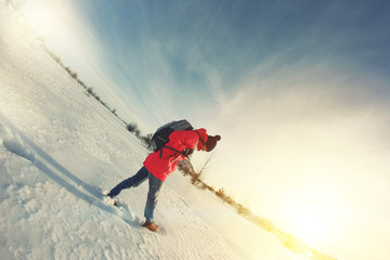 Woman traveler in bright winter jacket goes on a snowy field on a sunny day. Lens flare effect