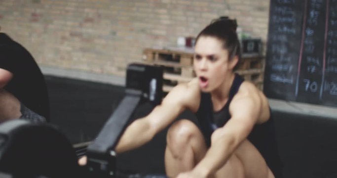 Fit man and woman exercising in gym, working out on rowing machine, giving high five after training