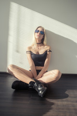 sensual blond girl in male boots sitting at sunlight on wall, toned image