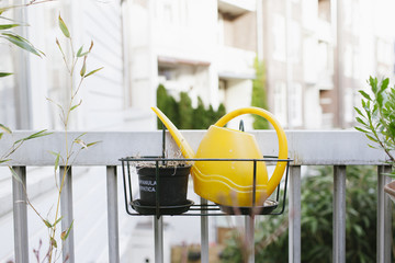 A yellow watering can on a balcony.