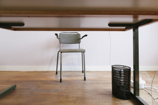 A vintage design chair standing behind a desk with a small black trash can on a wooden floor.