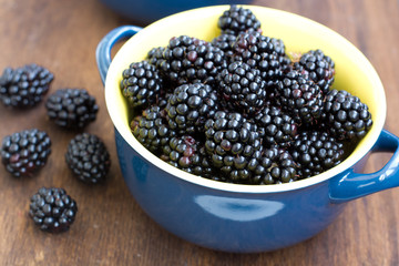 Blue dish full of fresh blackberry on wooden texture
