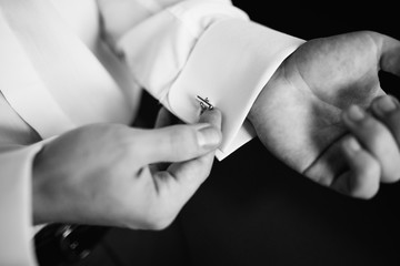 Black and white. Preparing for wedding. Groom buttoning cufflinks on white shirt before wedding. True men's accessory. Groom's clothes. Close up.