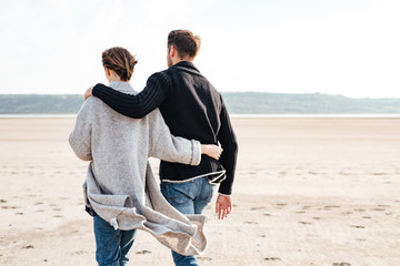 Back view of a young casual couple walking along beach