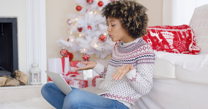 Cute young woman having a video chat on her laptop computer at Christmas as she relaxes on a sofa at home in front of the decorated Xmas tree.