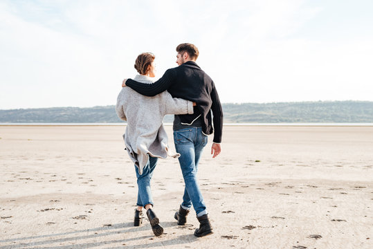 Back View Of A Young Casual Couple Walking Along Beach