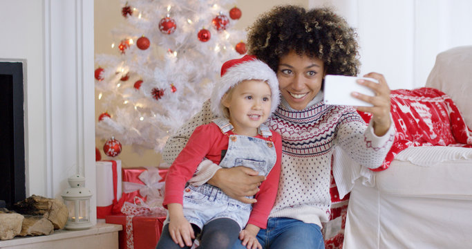 Woman and child posing for camera phone in front of white Christmas tree decorated with red ornaments