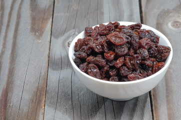 Dried grapes in white cup on wooden floor.