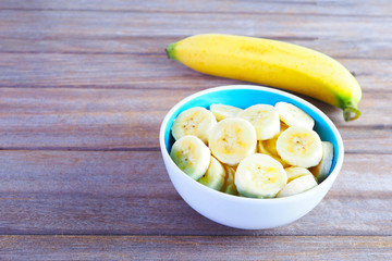 Close up of a bowl of sliced banana on a wooden background.