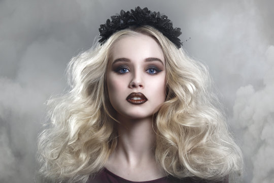 Beauty portrait of a beautiful young blonde woman with gothic make-up and decorative wreath in a puff of smoke.