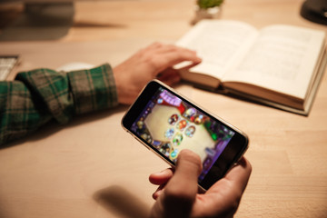 Man reading book and playing videogames on cell phone