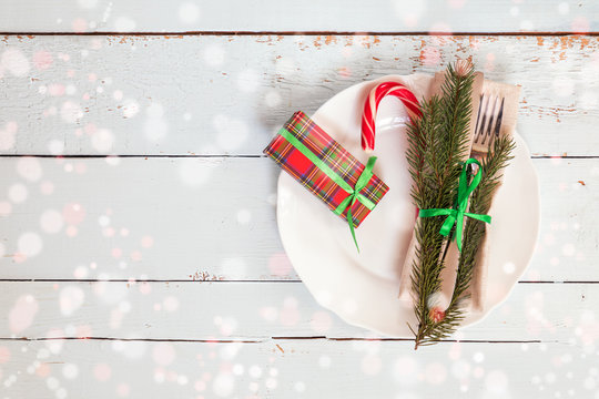 Country style christmas decoration. White empty plate, red apple and Christmas cookies with fir tree, candy, fork and knife tied with a green ribbon on light wooden background.