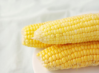 Ears of mature yellow corn on a white plate on a light background. Corn.