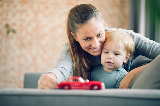 Mom And Her Toddler Son Plays With Red Car In Their Cosy Living Room