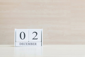 Closeup surface white wooden calendar with black 2 december word on blurred brown wood desk and wood wall textured background with copy space , selective focus at the calendar