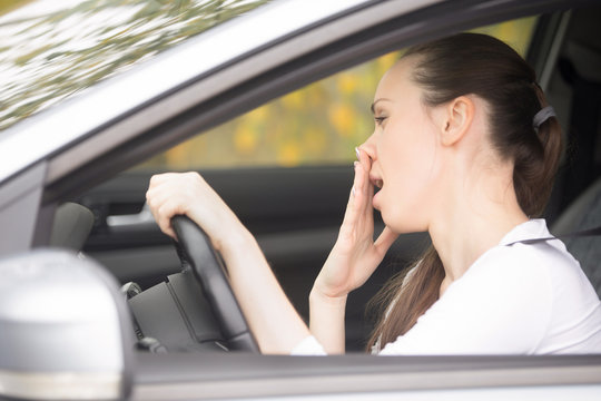 Young woman fell asleep during car ride, can't concentrate or feeling ill. Lady driver leaning on steering wheel, suffering whether from alcohol, poor sleep, new medication, or having horrible cold