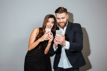 Happy cheerful couple in smart wear using mobile phones