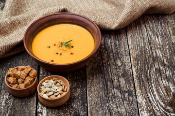 Bowl of pumpkin soup with bread crouton on dark wooden table.