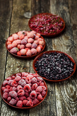 Frozen berries in bowls on wooden background. Selective focus.