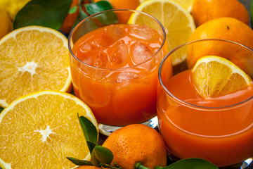 Healthy fresh citrus juice (two glasses), oranges, tangerines, lemons, ice, leaves.  Love for a healthy raw food concept