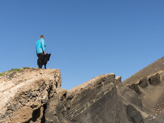 Man standing on a cliff with his black German Shepherd.