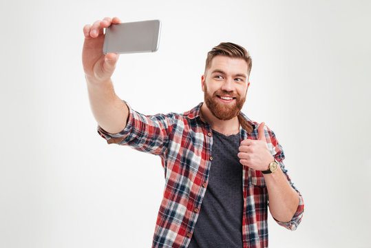 Cheerful bearded man taking selfie and showing thumbs up gesture