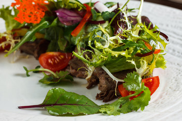 Vegetable salad menu for the restaurant in a large white plate on a white table cloth on a wooden table. Salad on the table with knife and fork. Svezhive vegetables.