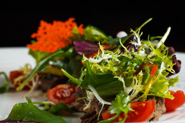 Vegetable salad menu for the restaurant in a large white plate on a white table cloth on a wooden table. Salad on the table with knife and fork. Svezhive vegetables.