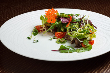 Vegetable salad menu for the restaurant in a large white plate on a white table cloth on a wooden table. Salad on the table with knife and fork. Svezhive vegetables.