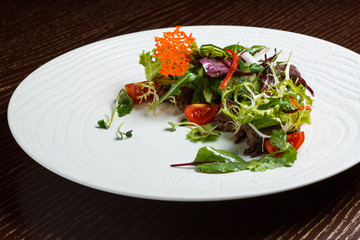 Vegetable salad menu for the restaurant in a large white plate on a white table cloth on a wooden table. Salad on the table with knife and fork. Svezhive vegetables.