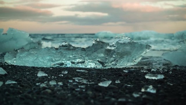 Dolly shot of ice and ocean waves at diamond beach in Iceland during sunset
